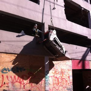 Behind site safeties back they drag a small skid steer up a building wall